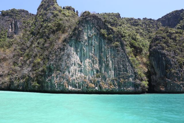 Stunning view of majestic limestone cliffs rising above clear turquoise water, likely in a tropical location in Thailand. Ideal for use in tourism promotions, travel blogs, adventure pages, nature documentaries, and coastal conservation materials.