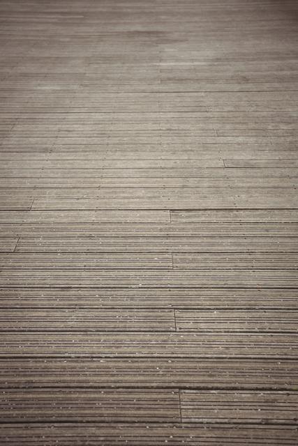 This image showcases a close-up view of a textured paving stone road, filling the entire frame. The detailed surface and pattern make it ideal for use in architectural presentations, urban design projects, or as a background for various graphic design purposes. The neutral gray tones and horizontal lines add a modern and clean aesthetic, suitable for websites, brochures, and advertisements related to construction, landscaping, and urban planning.