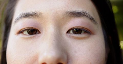 Midlife asian woman gazing closeup with freckled skin, natural light and soft bokeh