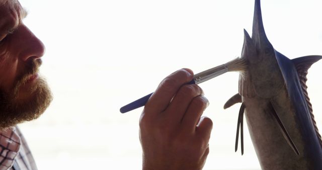 Man is carefully brushing a swordfish, possibly as part of conservation efforts or specimen preparation. Useful for topics related to animal care, wildlife preservation, detailed work, and educational content.