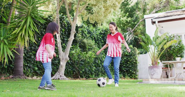 Image of happy asian mother and daughter playing soccer in garden. Family, motherhood, relations and spending quality time together concept digitally generated image.