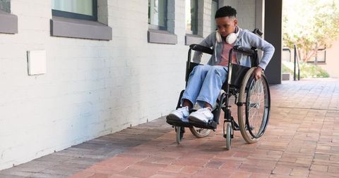 African american teen pushing wheelchair along campus walkway wearing hoodie and headphones
