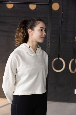 Young woman standing beside gym rings wearing hoodie and leggings facing right, focused workout port