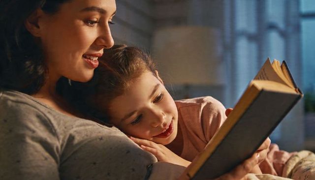Mother reading bedtime story while cradling daughter in cozy bedroom light
