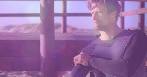 Man Adjusting Wetsuit on Deck Overlooking Sandy Dunes