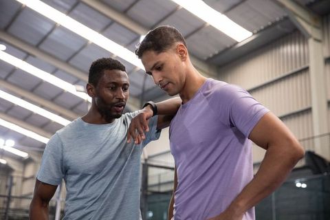 Two diverse male athletes coaching and listening after workout in indoor sports facility