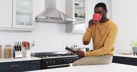 Man Sipping Coffee Holding Tablet in Modern Kitchen