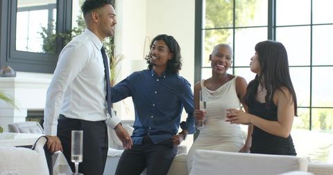 Friends celebrating with champagne in modern living room, toasting in cocktail attire