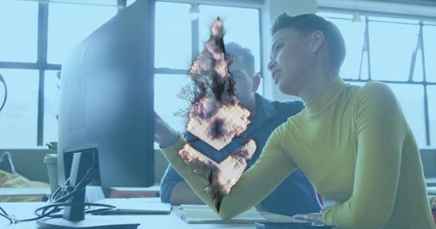 Collaborating colleagues pointing at monitor in modern office with grunge burn overlay