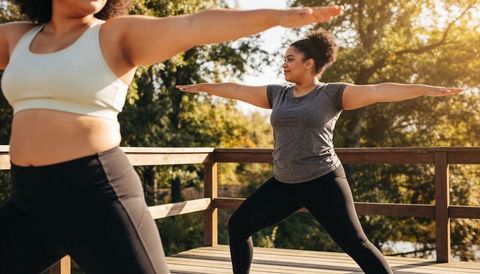 Women practicing warrior pose on sunlit wood deck during outdoor yoga session