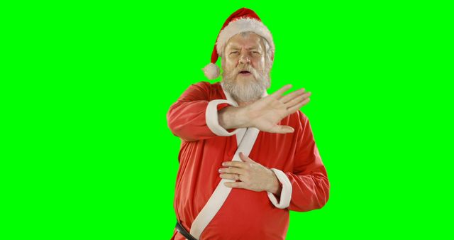 Elderly man dressed as Santa Claus gesturing to stop in front of a green screen background. Useful for holiday advertisement, digital animations, Christmas event promotions, festive greeting cards, and social media marketing.