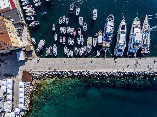 Aerial perspective showing numerous boats docked closely together in a Mediterranean harbour, highlighting the vibrant maritime activity and clear blue water. Surrounding buildings and smooth stone dock are visible, indicating an urban coastal area perfect for tourism and leisure activities. Great for use in travel brochures, tourism websites, and advertisements for Mediterranean destinations or maritime services.
