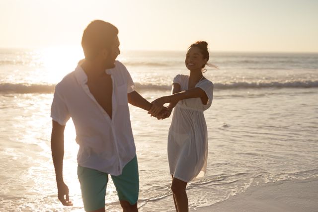 Romantic couple walking hand in hand along the beach during sunset, enjoying each other's company. Perfect for travel brochures, romantic getaway promotions, lifestyle blogs, and advertisements focusing on relationships and leisure activities.