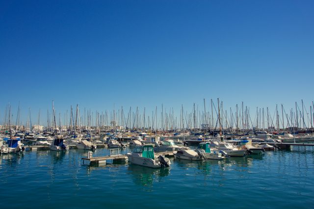 This image shows a marina filled with numerous sailboats and motorboats docked on calm water under a clear blue sky. Ideal for use in travel blogs, tourism promotions, maritime industry websites, and lifestyle magazines. The tranquil setting and abundance of boats highlight nautical themes and leisure activities.