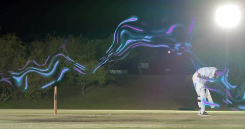 Bending cricketer holding bat on night pitch with neon trails floodlight long exposure