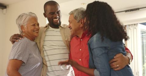 Multigenerational diverse family hugging and laughing in sunlit living room