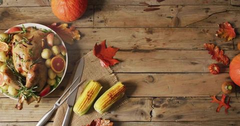 Displaying roasted turkey platter with grilled corn and pumpkins on rustic wooden table