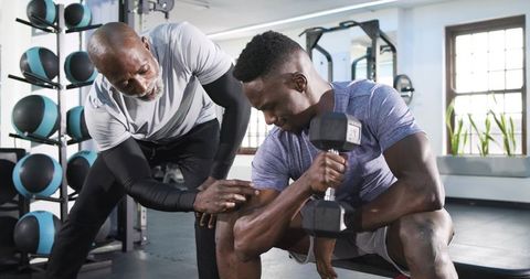 African american man doing dumbbell curl with trainer's guidance in gym