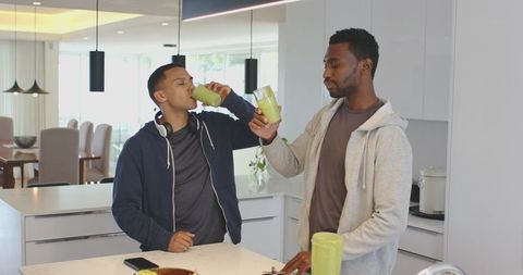 Multiracial men toasting green smoothies at minimalist kitchen island morning routine