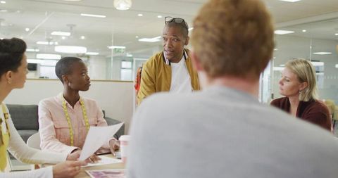 Multicultural creative team leading design presentation in open office with mockups