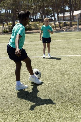 Diverse girls practicing soccer on sunlit turf controlling ball during youth team training