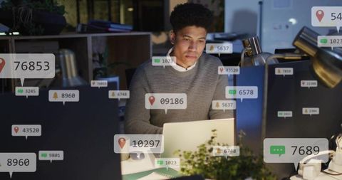 Working late analyzing data with notifications on laptop in open-plan office at night