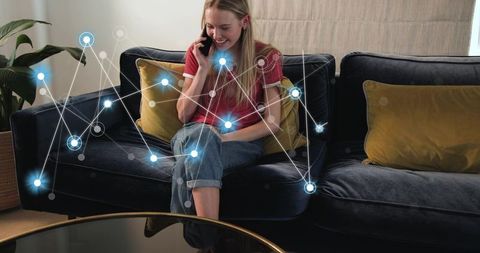 Young woman talking on smartphone on sofa with glowing network overlay in cozy living room