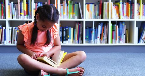 Young girl reading storybook on library floor embracing learning