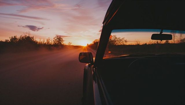 Driving into sunset on dusty country road with side mirror and dashboard silhouette