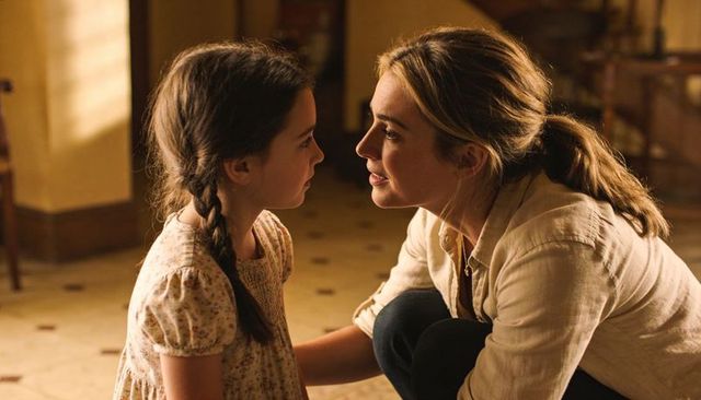 Crouching mother leaning toward daughter sharing gentle conversation on sunlit tiled floor