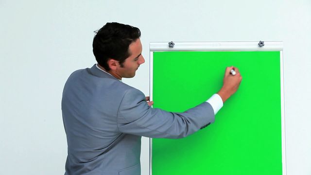 Businessman writing on a green screen board during a presentation. Ideal for illustrating business presentations, professional training, corporate meetings, and workshop scenarios.