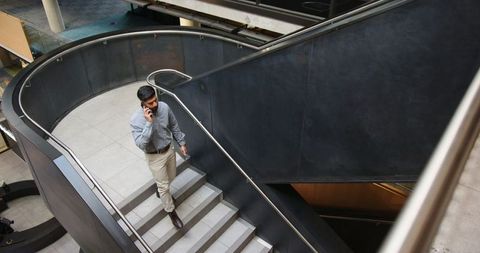Businessman Walking up Modern Curved Stairs in Office Atrium