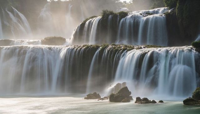 Cascading multi-tier waterfall over layered rock terraces bathed in golden mist