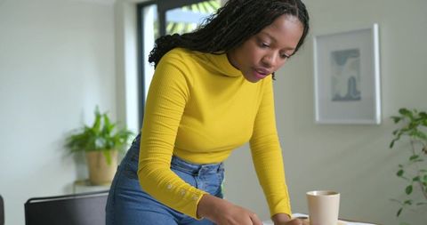 African american woman leaning over home office desk sorting papers for productivity
