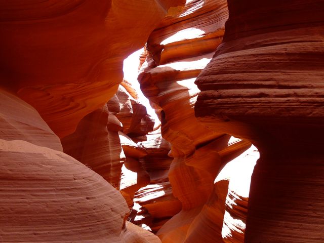 Sunlight filtering through narrow sandstone canyon creates contrasting shadows and highlights on curving rock walls. Sharp edges and smooth curves showcase unique erosional patterns of ancient landscape, ideal for nature, geology, and travel content in promotional materials, websites, and educational resources.