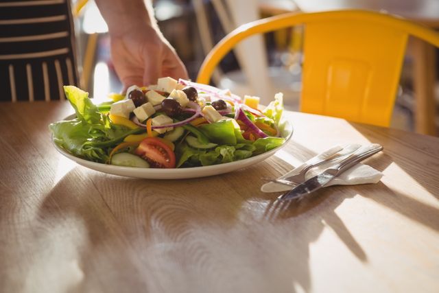 Cropped hand of waiter serving salad on wooden table in cafe