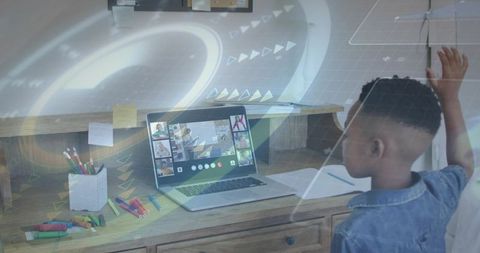 Child raising hand during remote classroom on laptop at home study desk with markers