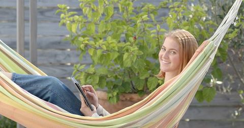 Woman Relaxing on Pastel Striped Hammock Using Tablet Outdoors