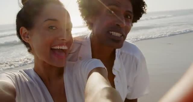 Couple enjoying a sunny day at the beach, capturing moments with a selfie. Ideal for lifestyle, travel promotions, summer vacation advertisements, and social media content highlighting fun and happiness at the seaside.