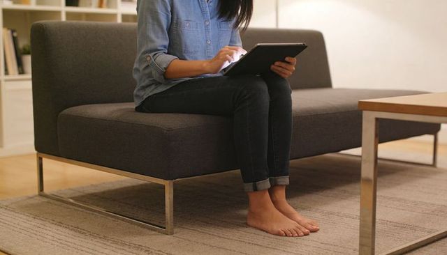 Woman using tablet on dark gray sofa, casual denim outfit in minimalist living room