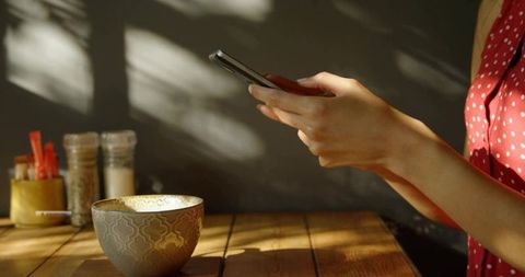 Woman Using Smartphone at Cozy Table with Ceramic Bowl