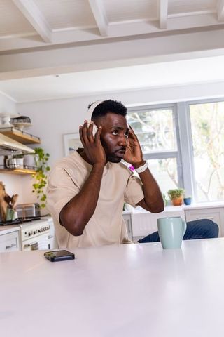 African american man adjusting white headphones during morning at bright kitchen counter