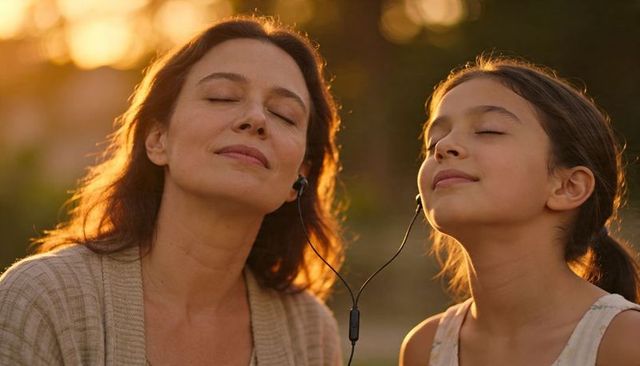Mother daughter sharing earphones during golden hour outdoors, bonding and relaxing