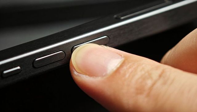 Pressing fingertip on brushed metal side button of smartphone close-up for tactile control