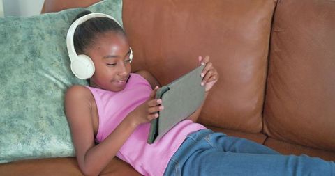 African american girl relaxing on couch using tablet and headphones for home learning