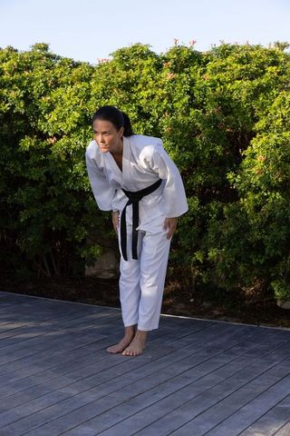 Martial artist woman in gi bowing outdoors on wooden deck