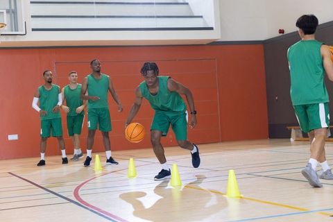 Multiracial men's basketball team practicing precision dribbling drill on indoor court