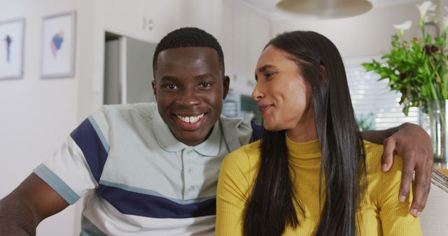 Image of happy diverse couple making image call smiling and waving to camera in kitchen. Communication, happiness, domestic life and inclusivity concept.