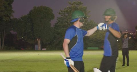 Night cricket teammates celebrating run with fist bump on floodlit outfield