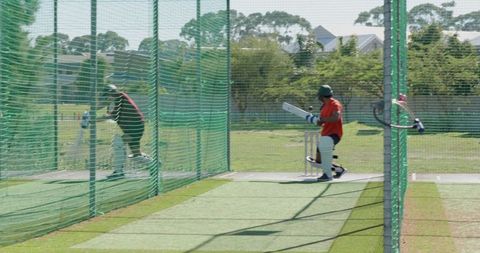 Cricket practice nets batsman in orange shirt holding bat near stumps